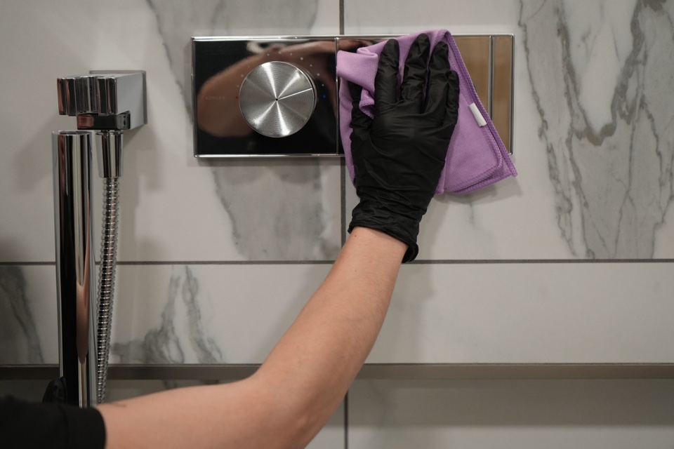 A gloved hand with a lavender cloth polishing chrome shower controls