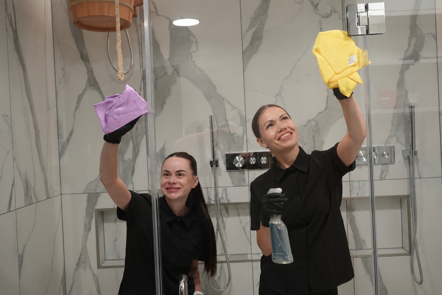 Two BroomStar cleaners washing a glass shower door with cloths and spray