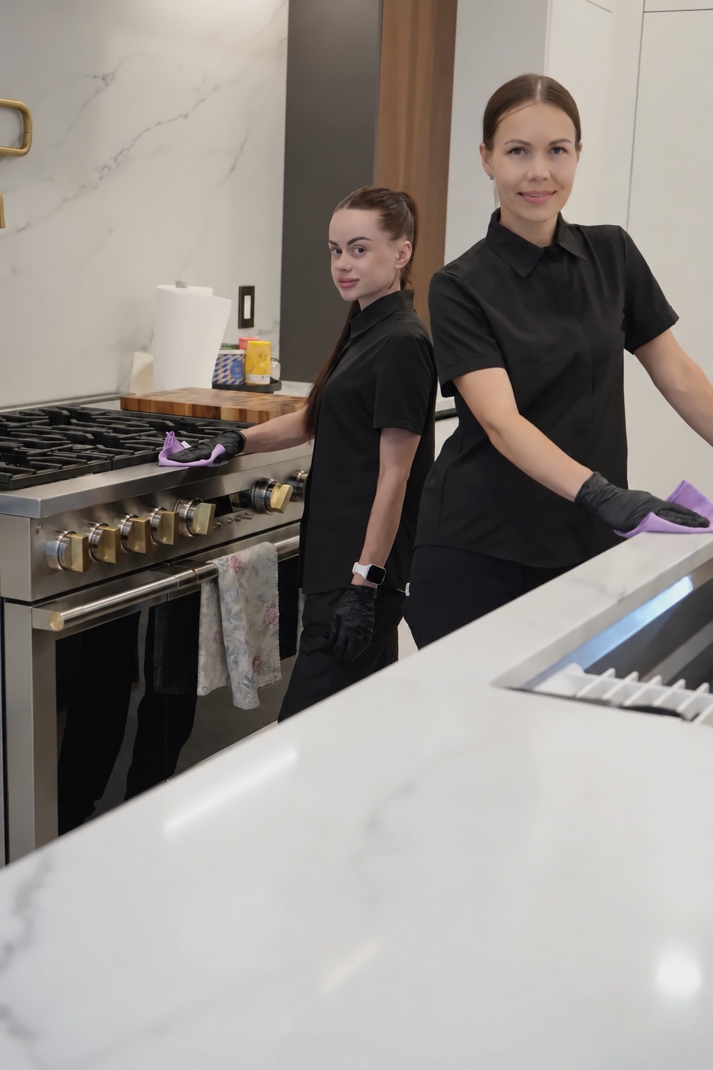 Two cleaners at a kitchen range, wiping the stovetop and the counter